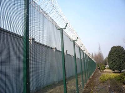 Green vinyl-coated prison fence with razor wire on top.