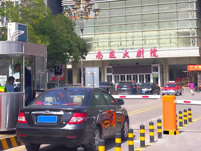 A car is passing through the entrance of theatre with steel traffic cylinder.