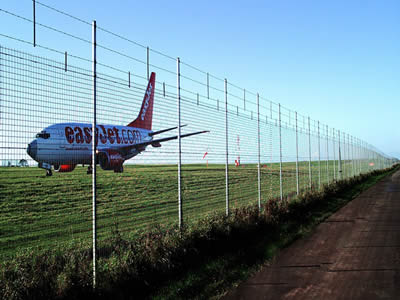 A plane is over airport runway with airport welded wire fence.